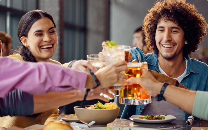 A couple of smiling millennial adults toasting with beverages together. 