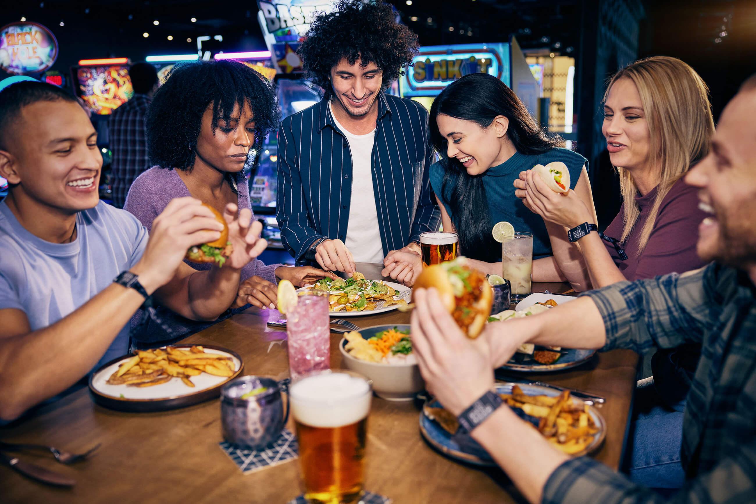 Group of millennial adults around a bar table eating a variety of food.