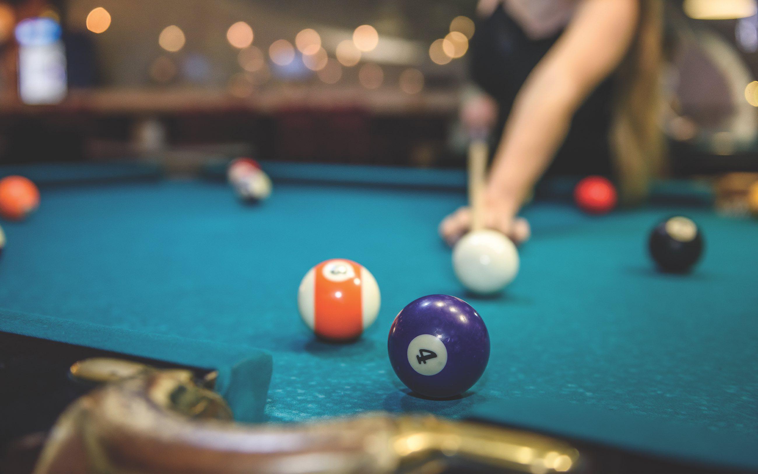 A woman playing pool on a billiards table attempting to sink the 4 ball. 