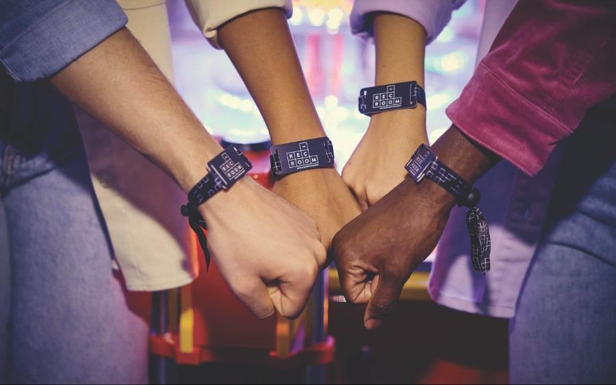 Four hands wearing gaming wristbands, fist bumping. 