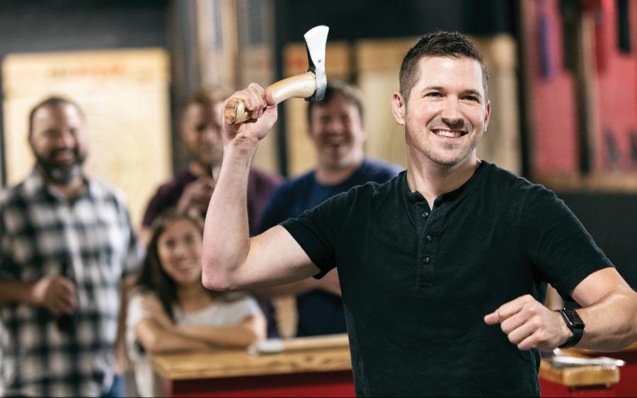 Man throwing an axe at a target while friends watch. 