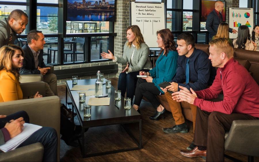 A group of co-workers discuss business around a coffee table in a lounge setting. 